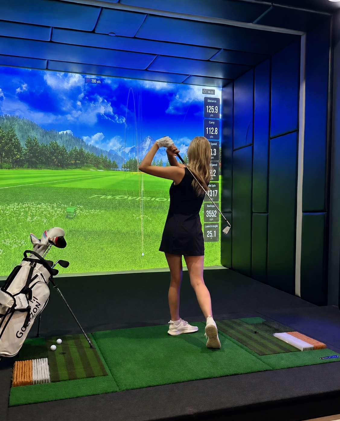 Golfer finishing a swing in a real Lounge X GOLFZON simulator bay
